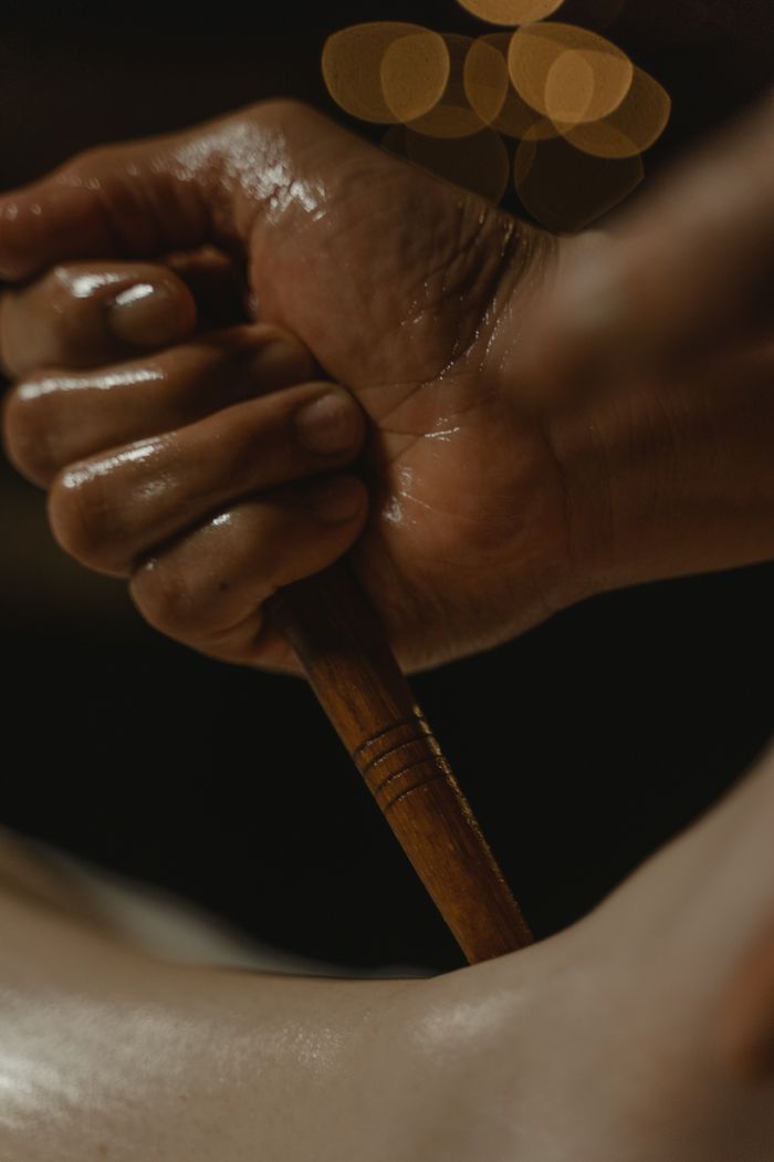 About A close-up of a hand holding a wooden massage tool, set against a dark background.